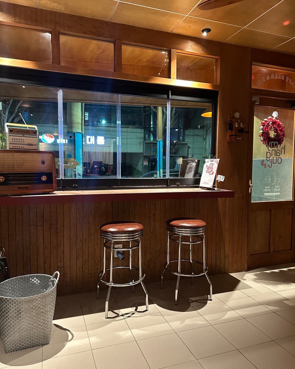 부산광역시 중구 마이행아웃 맥주 호프의 창가 다찌석. 가죽 시트 의자와 목재 카운터, 빈티지 라디오가 배치된 1인 혼술 공간으로 조명이 바닥을 비추는 야간 실내 구성