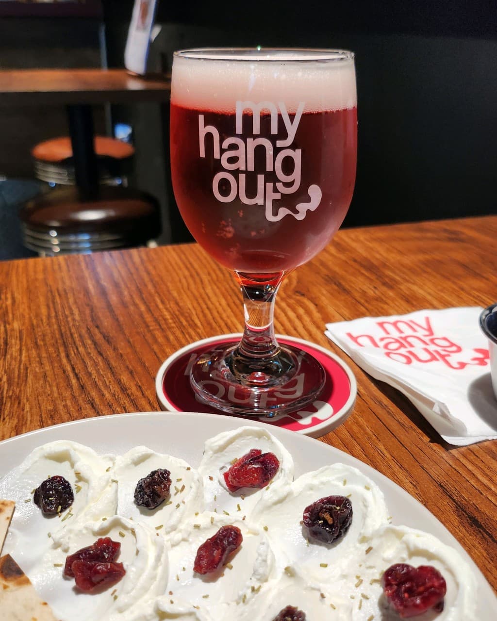 부산광역시 중구 맥주 호프 마이행아웃의 나무 테이블 위 로고 잔에 담긴 붉은 맥주와 크랜베리 크림치즈. 조명 아래 1인 혼술을 즐기는 상황.