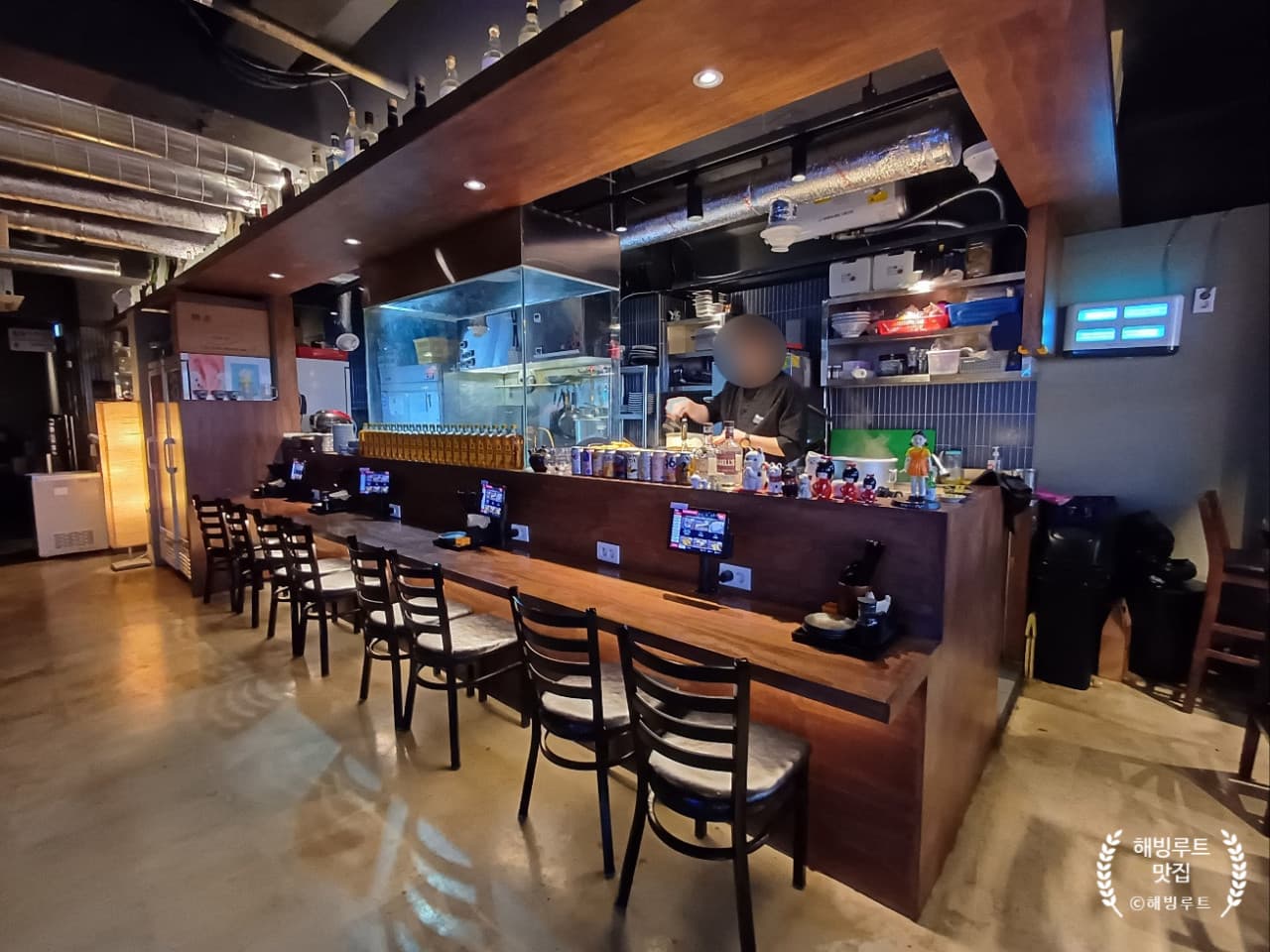 부산광역시 중구 요리주점 히노카오뎅 남포점의 긴 원목 다찌석과 좌석별 주문 태블릿. 상단 조명이 비추는 1인 카운터석으로 구성된 혼술 전문 공간.