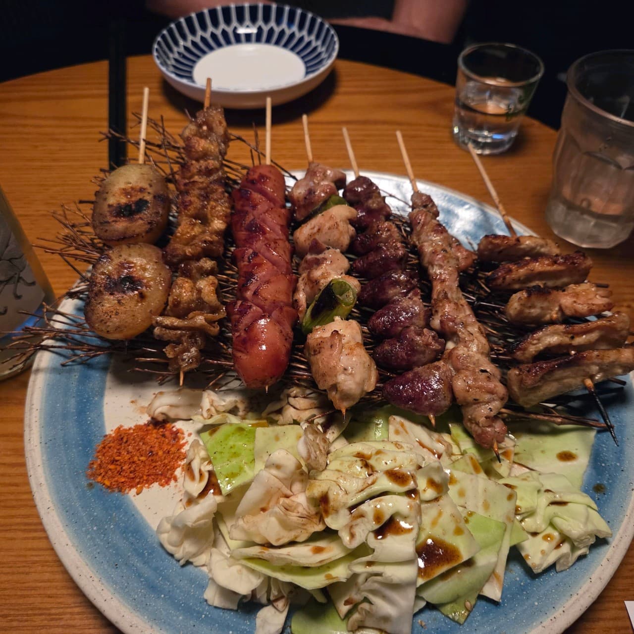 부산광역시 중구 도코로 남포동본점 이자카야 다찌석 조명 아래 차려진 1인 모둠 꼬치구이 세트와 소스가 뿌려진 양배추를 곁들인 혼술 상황