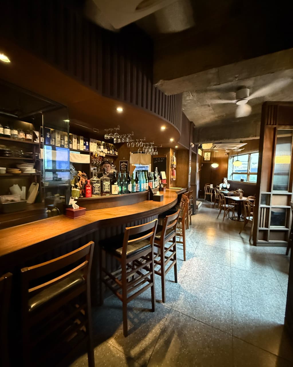 부산광역시 중구 도코로 남포동본점 이자카야. 하이라이트 조명이 비추는 나무 다찌석과 벽면에 진열된 술병들로 구성된 1인 혼술 공간.