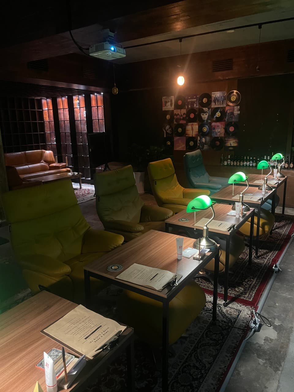 부산광역시 중구 맥주 호프 풍악 - 초록색 스탠드 조명이 켜진 1인용 테이블과 소파 좌석. 벽면 LP 판과 낮은 채도의 실내 조명 아래 혼술을 즐기는 상황.