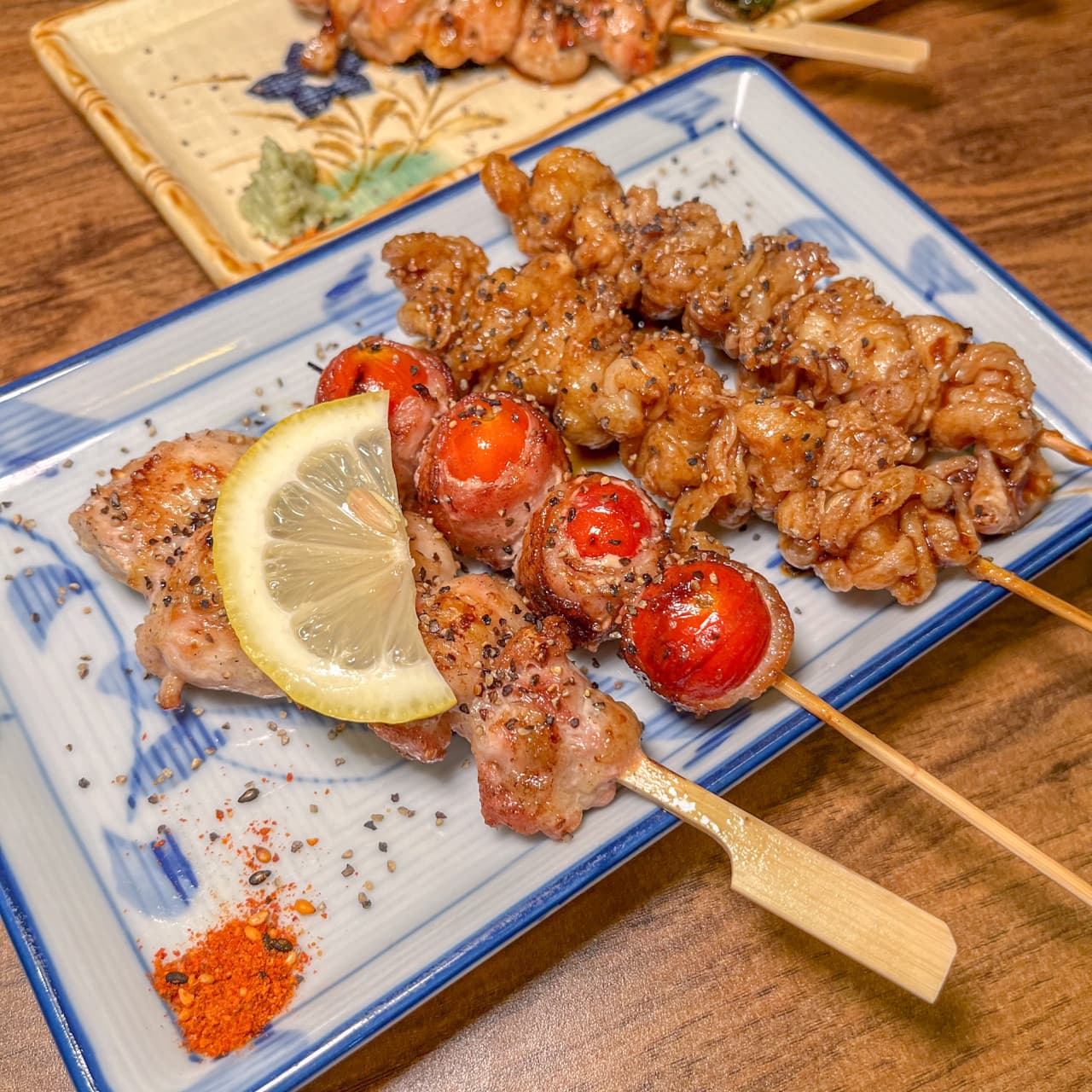 부산광역시 중구 이자카야별하 이자카야 다찌석 1인 혼술. 조명 아래 닭껍질과 토마토 베이컨 꼬치구이, 레몬 슬라이스가 차려진 목재 테이블 상차림.