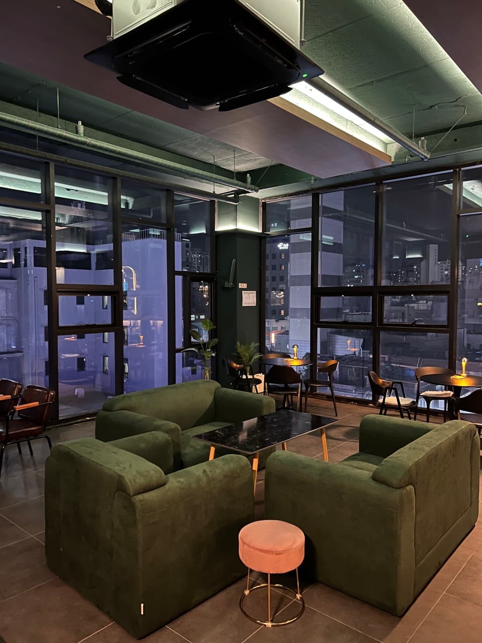 부산광역시 중구 선셋라운지 바(Bar) - 시티뷰 통창 앞 초록색 벨벳 소파와 대리석 테이블, 1인 혼술객을 위한 은은한 스탠드 조명 좌석