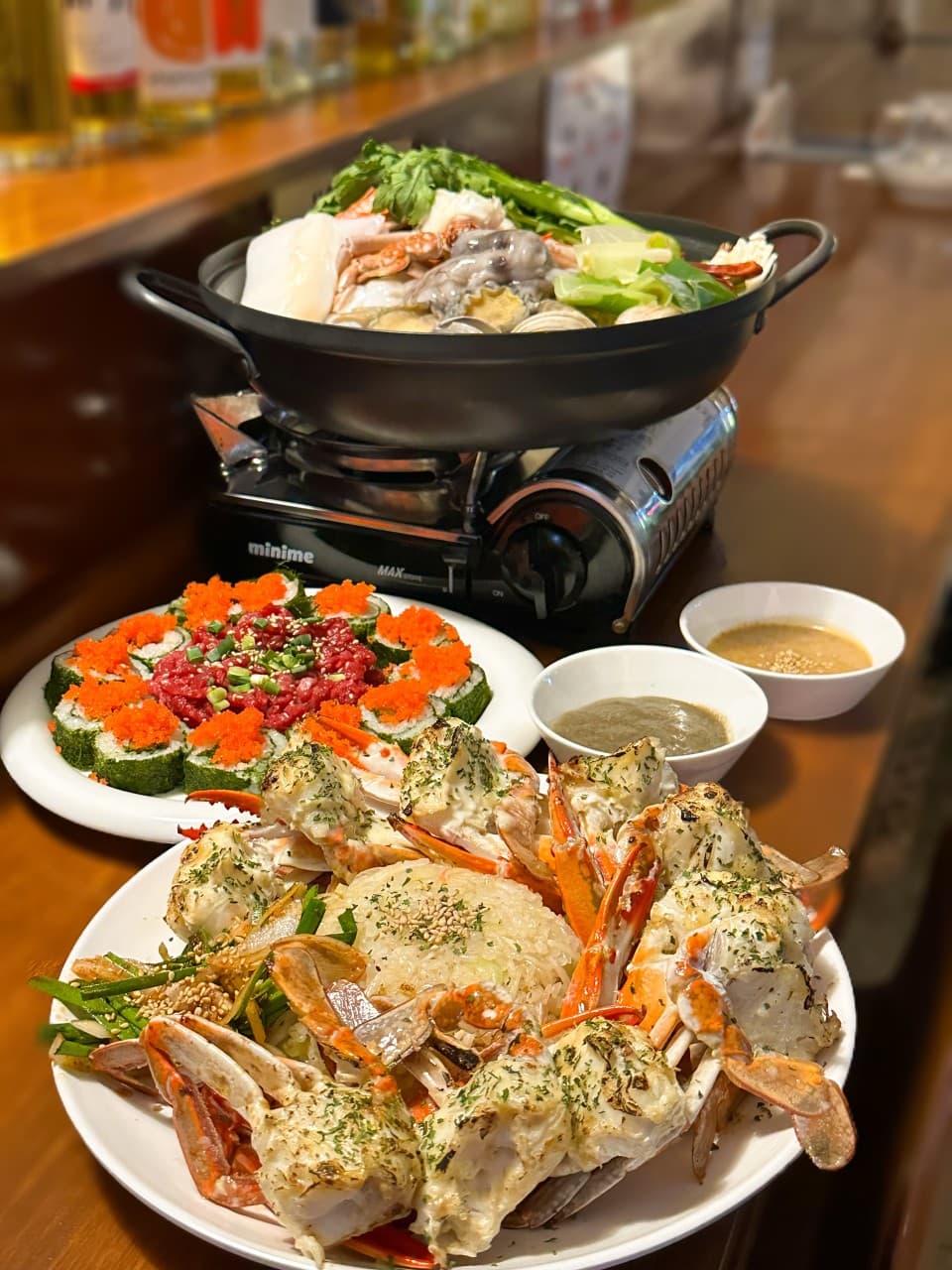 경상남도 창원시 요리주점 오로시 나무 다찌석 위 해물탕과 육회 김밥, 게 요리가 차려진 1인 혼술 상황. 따뜻한 색감의 조명 아래 해산물 안주의 질감이 돋보이는 구성.