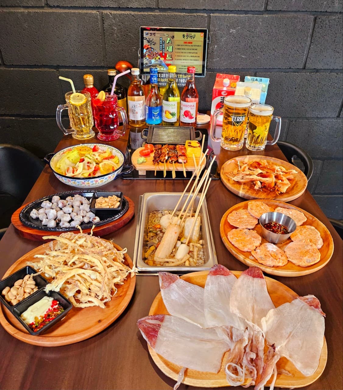 경상남도 창원시 이자카야 꼬뎅 다찌석 상차림. 중앙의 어묵탕과 꼬치구이, 바삭한 건어물 안주 옆으로 생맥주와 하이볼이 놓인 1인 혼술 상황.