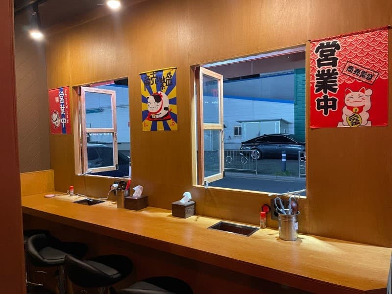 경상남도 창원시 이자카야 꼬뎅의 나무 다찌석과 핀 조명이 설치된 1인 좌석. 창문 너머로 저녁 거리 풍경이 보이는 카운터석에서 혼술하는 상황을 나타냄.