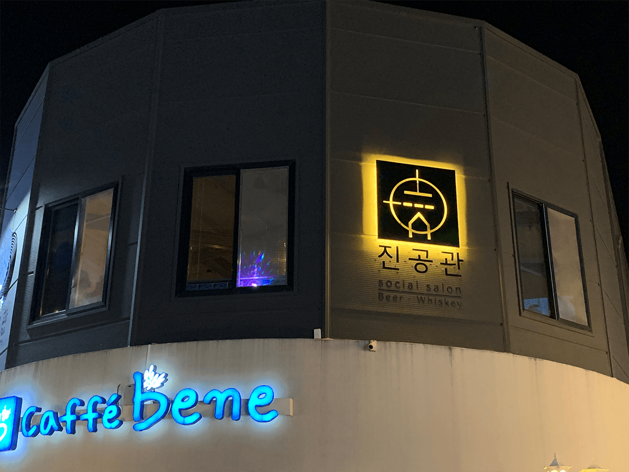 경상남도 사천시 진공관의 노란 조명 간판이 빛나는 밤 거리. 맥주와 위스키를 마시는 1인 혼술 공간이자 기타 소셜 살롱의 어두운 건물 외벽과 창문의 빛이 대비되는 전경.