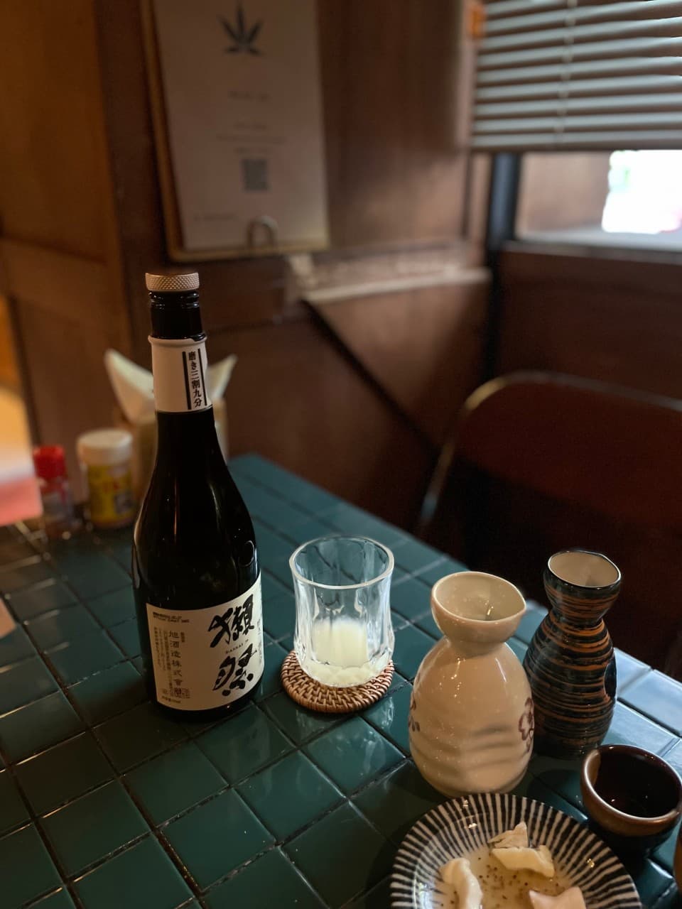 경상남도 사천시 이자카야 야키토리 낙원 다찌석에서 초록색 타일 테이블 위 닷사이 사케와 도자기 술병을 두고 즐기는 1인 혼술 상황