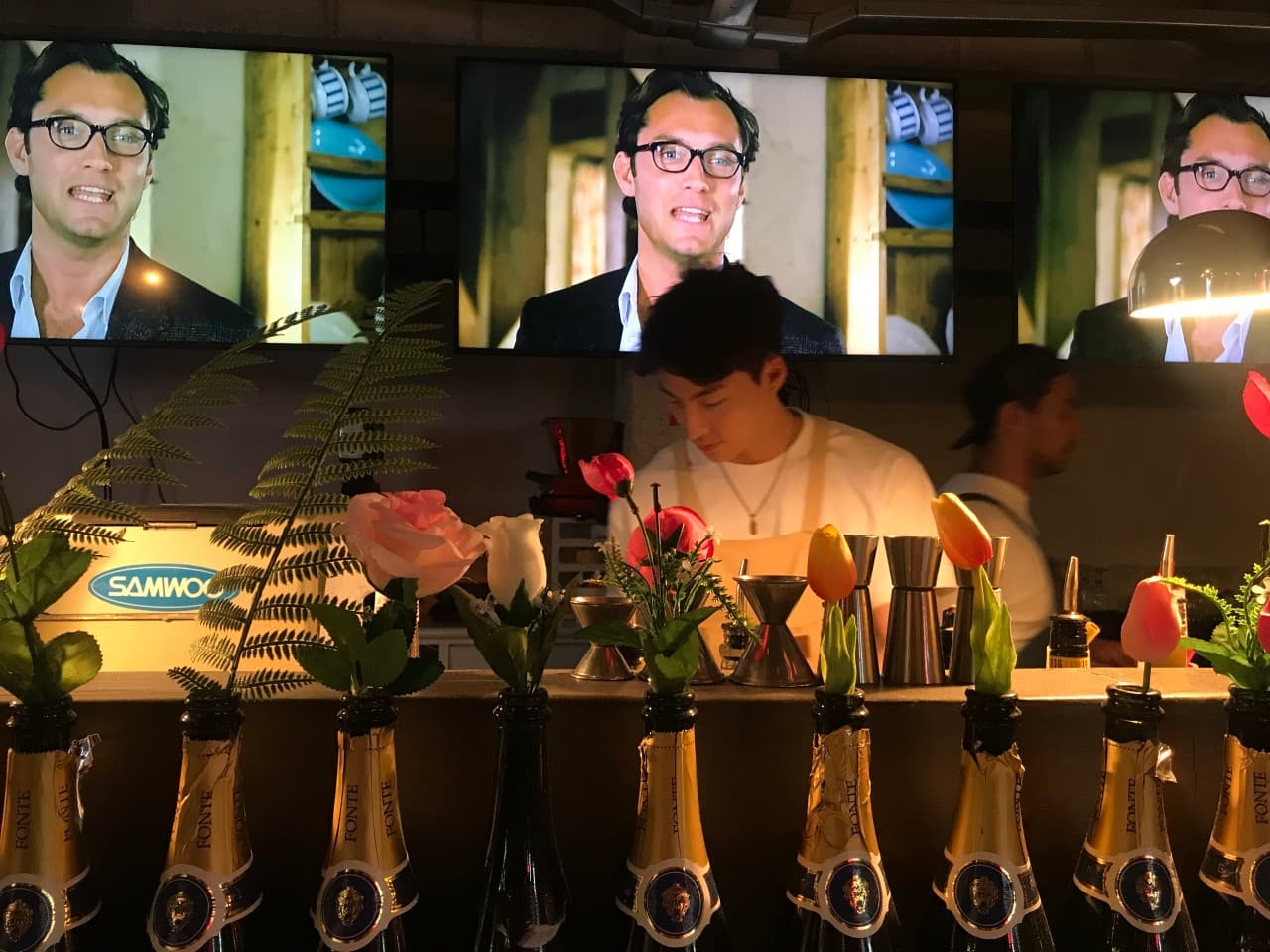 경상남도 진주시 파머스 맥주 호프 - 꽃이 꽂힌 술병들이 나열된 다찌석 너머 바텐더와 대형 스크린이 위치한 1인 혼술 전용 공간