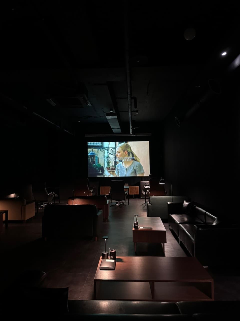 경상남도 진주시 와인바 스몰그룹 진주. 대형 스크린 영화 상영과 낮은 조도의 테이블 조명이 비치는 1인 가죽 소파 좌석이 배치된 혼술 공간.
