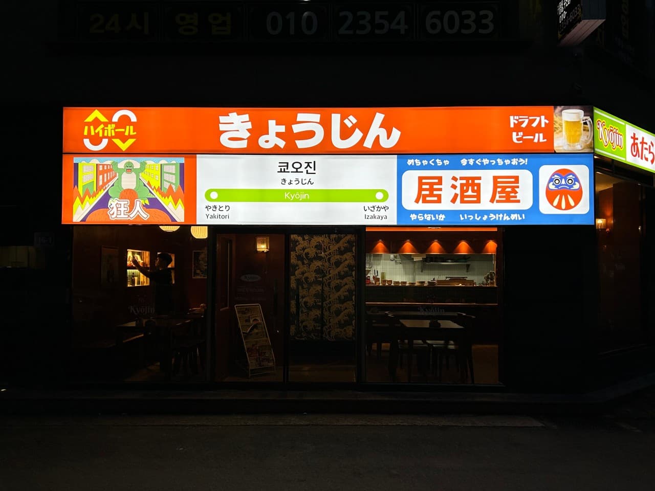 경상남도 진주시 이자카야 쿄오진 진주 - 주황색 기차역 테마 간판 아래 다찌석과 1인 좌석이 배치된 조명이 켜진 혼술 매장 전경