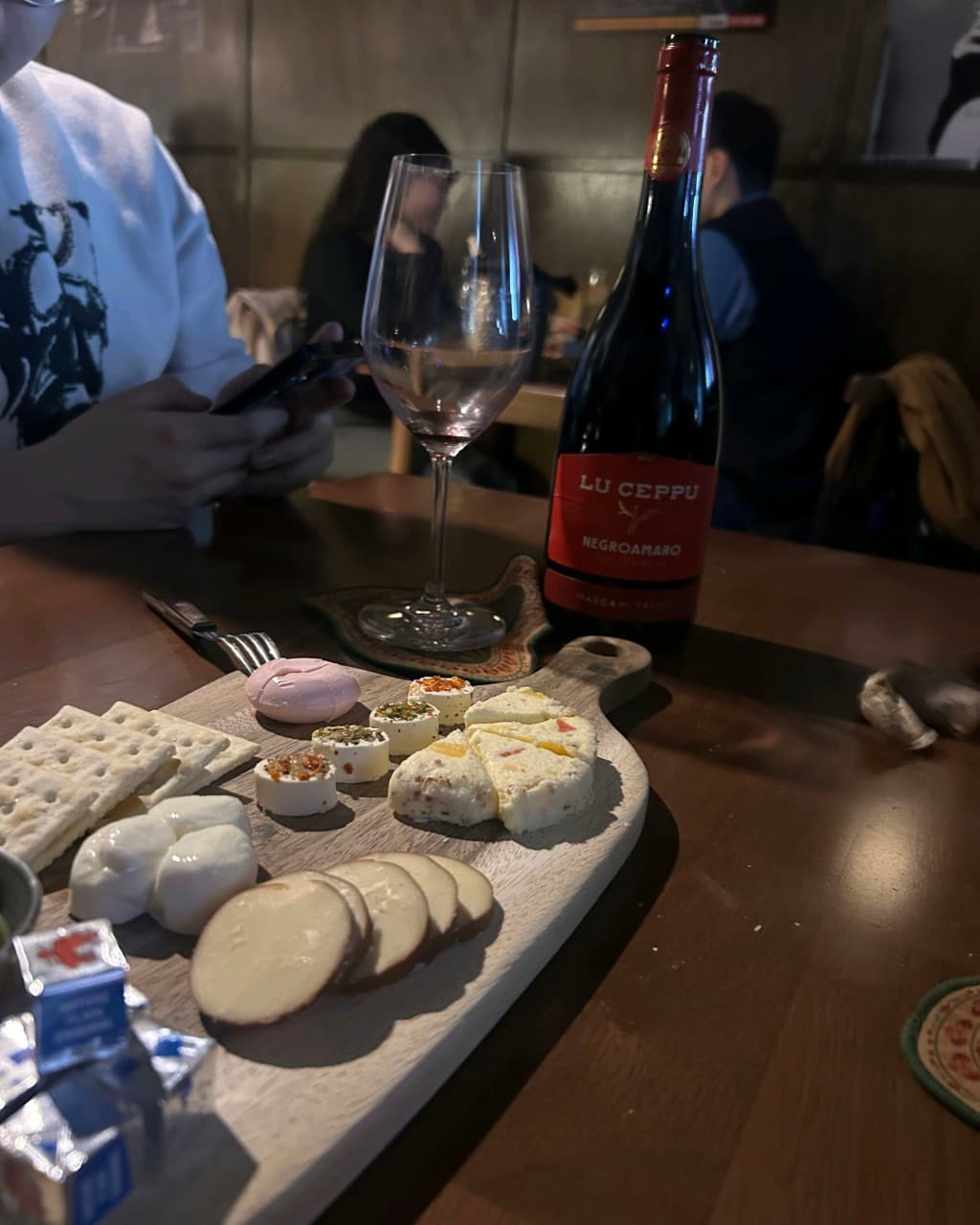 서울특별시 송파구 낭만LP바 잠실방이점 바(Bar)의 낮은 조도 아래 목재 테이블 위 레드 와인과 치즈 플래터. 혼술 상황을 보여주는 다양한 질감의 치즈와 크래커가 담긴 1인 플레이트.