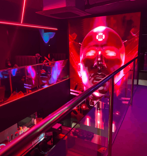 서울특별시 송파구 나쉬펍 잠실방이점 맥주 호프. 붉은 조명과 대형 미디어 월이 설치된 다찌석에서 혼술. 바 테이블과 1인석 좌석이 내려다보이는 복층 구조의 실내.