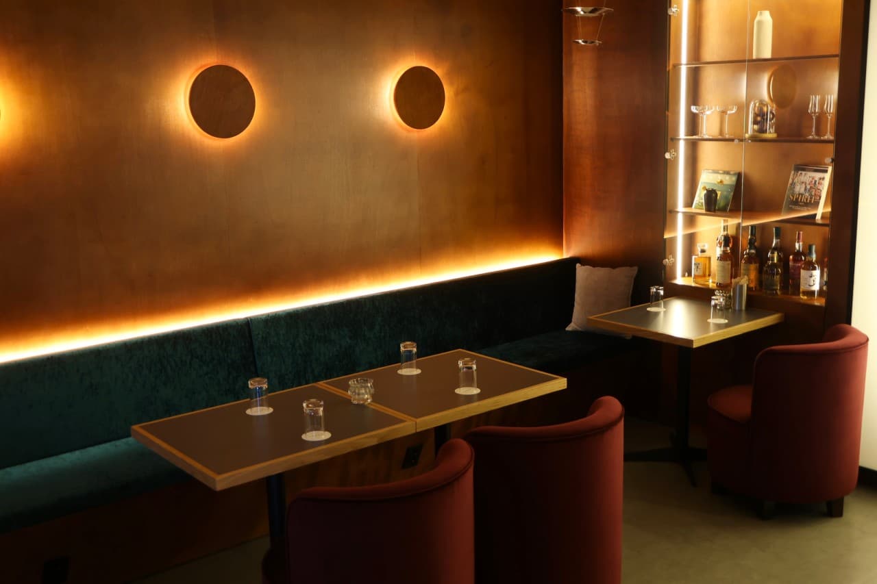 경상남도 진주시 슈럽 진주 바(Bar) - 주황색 간접 조명과 초록색 벨벳 소파, 위스키 진열장 옆 1인 테이블이 마련된 혼술 공간