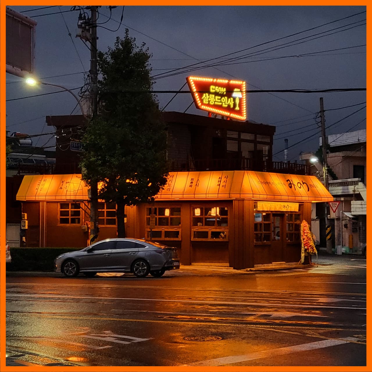 경상남도 진주시 미노리인사 진주 이자카야 - 주황색 조명이 켜진 외관과 다찌석 창가, 비 내린 밤 거리에서 1인 혼술을 즐기는 상황