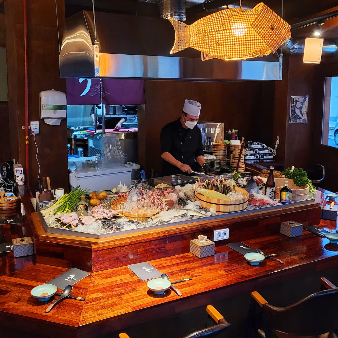 경상남도 진주시 미노리인사 진주 이자카야 - 물고기 조명 아래 1인 다찌석과 얼음 위 진열된 꼬치 재료들. 셰프가 직접 조리하는 카운터에서 즐기는 혼술 상황