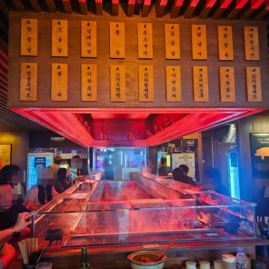 서울특별시 송파구 야키톤탄탄 잠실 이자카야 붉은 조명 아래 연기 피어오르는 다찌석. 나무 메뉴판이 배치된 1인 좌석에서 혼술을 하며 꼬치구이가 조리되는 상황.