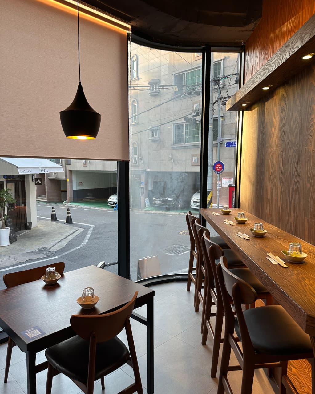 대전광역시 서구 이자카야 마포십번 대전서구의 1인 혼술 다찌석. 통창 너머 거리 풍경이 보이는 창가 자리와 황색 조명 아래 배치된 목재 테이블 세팅.