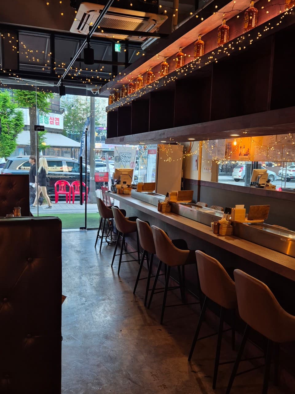 대전광역시 유성구 도리토리 대전봉명점 요리주점 내부. 전구 조명과 술병이 진열된 선반 아래 긴 다찌석과 높은 의자가 놓인 1인 혼술용 카운터 좌석 배치