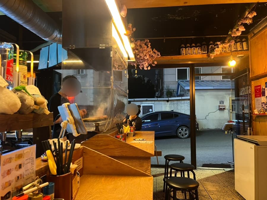 대구광역시 달서구 혼술 이자카야 토리아에즈 상인동 대구점 - 노란 조명 아래 다찌석과 블랙 스툴, 연기가 피어오르는 그릴 앞 바 테이블에서 즐기는 1인 식사