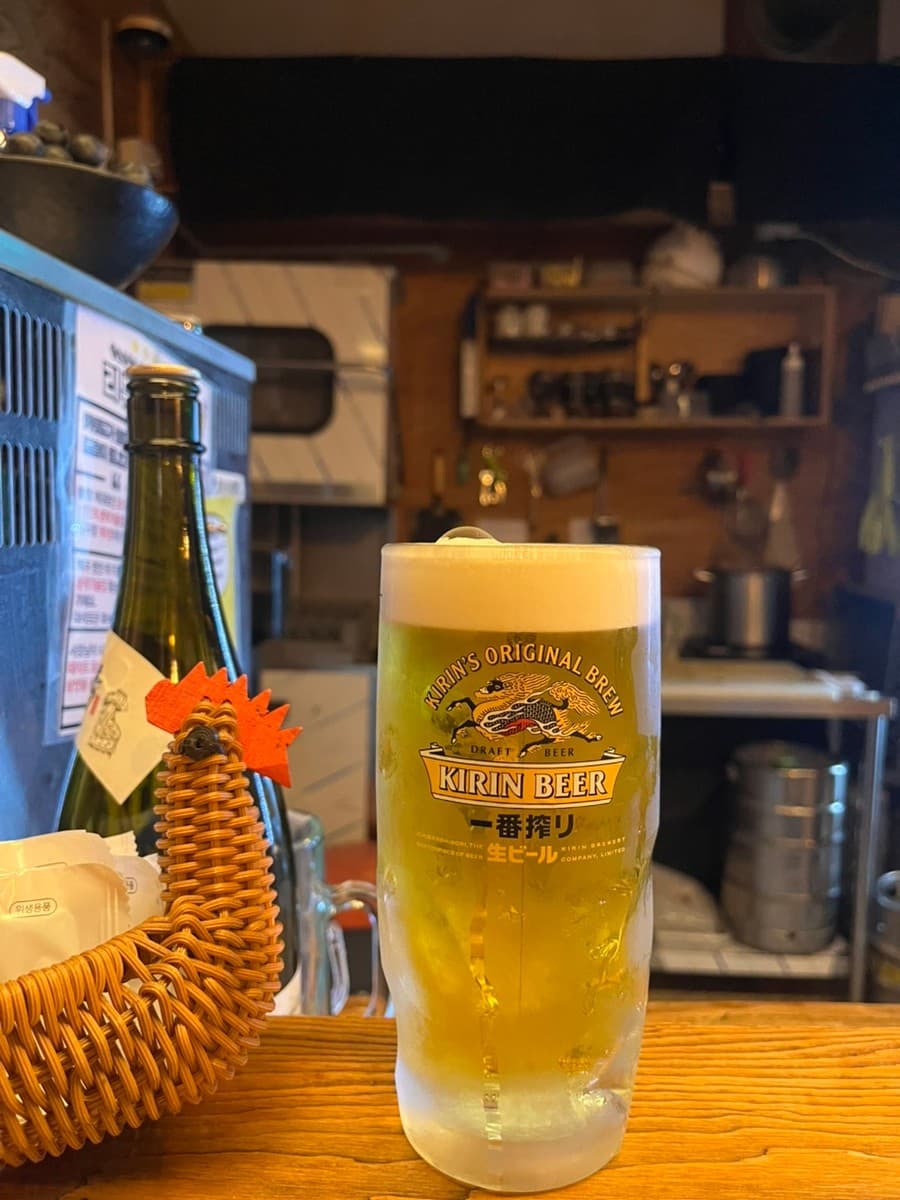 대구광역시 달서구 이자카야 토리아에즈 상인동 대구점 다찌석의 기린 생맥주. 낮은 조명 아래 주방을 배경으로 거품 덮인 잔이 놓인 1인 혼술 상황.