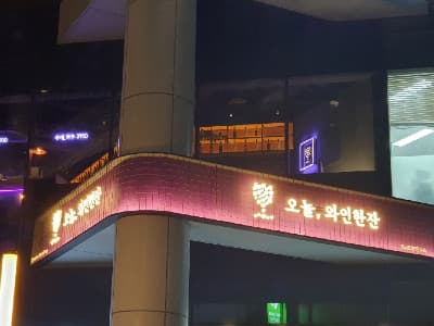 서울특별시 강남구 오늘와인한잔 강남역 외부 보라색 조명 아래 와인 병이 진열된 창가 다찌석이 보이며 1인 혼술에 적합한 공간을 보여줌.
