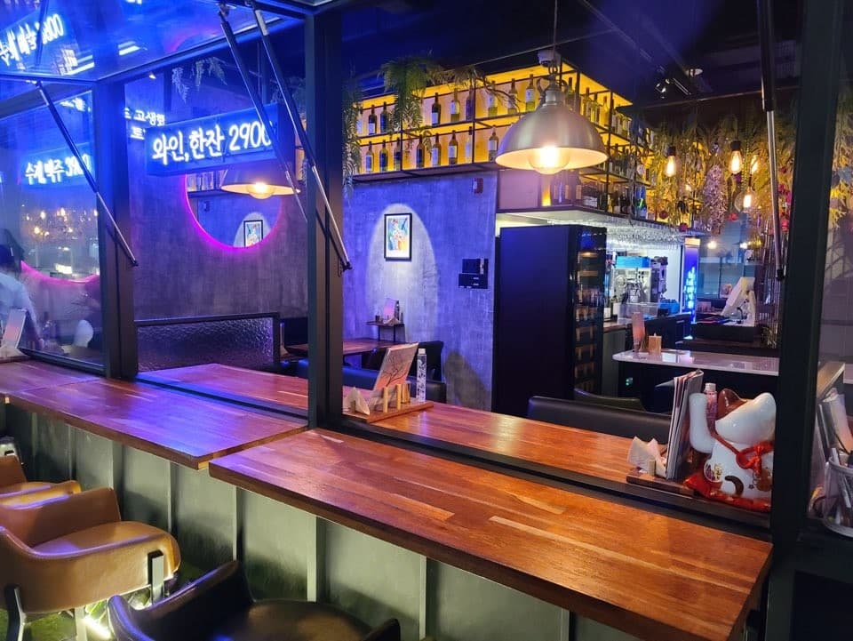 서울특별시 강남구 오늘와인한잔 강남역 혼술 와인 매장 내부. 보라색 네온과 노란 조명이 비치는 1인 다찌석 테이블 및 벽면에 진열된 와인병 구성