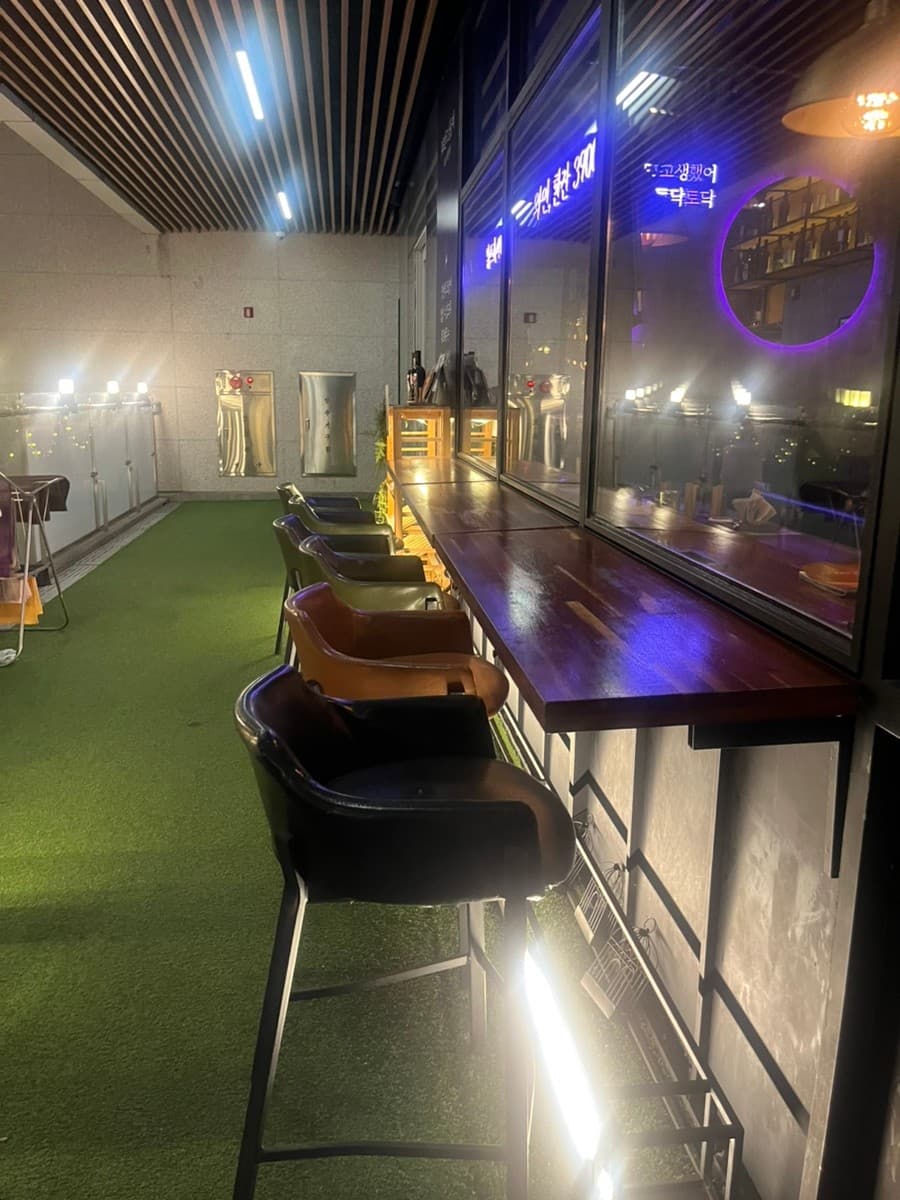 서울특별시 강남구 오늘와인한잔 강남역 와인 매장. 네온 사인이 비치는 유리창 앞 나무 다찌석과 1인용 의자가 나란히 놓인 테라스 혼술 공간.