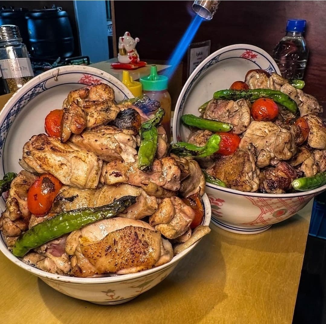 서울특별시 강남구 이자카야 쿄코코 신논현 다찌석에서 토치로 직화하는 1인 닭고기 덮밥. 구운 닭다리살과 꽈리고추의 질감이 강조된 목재 카운터석 혼밥 상황.