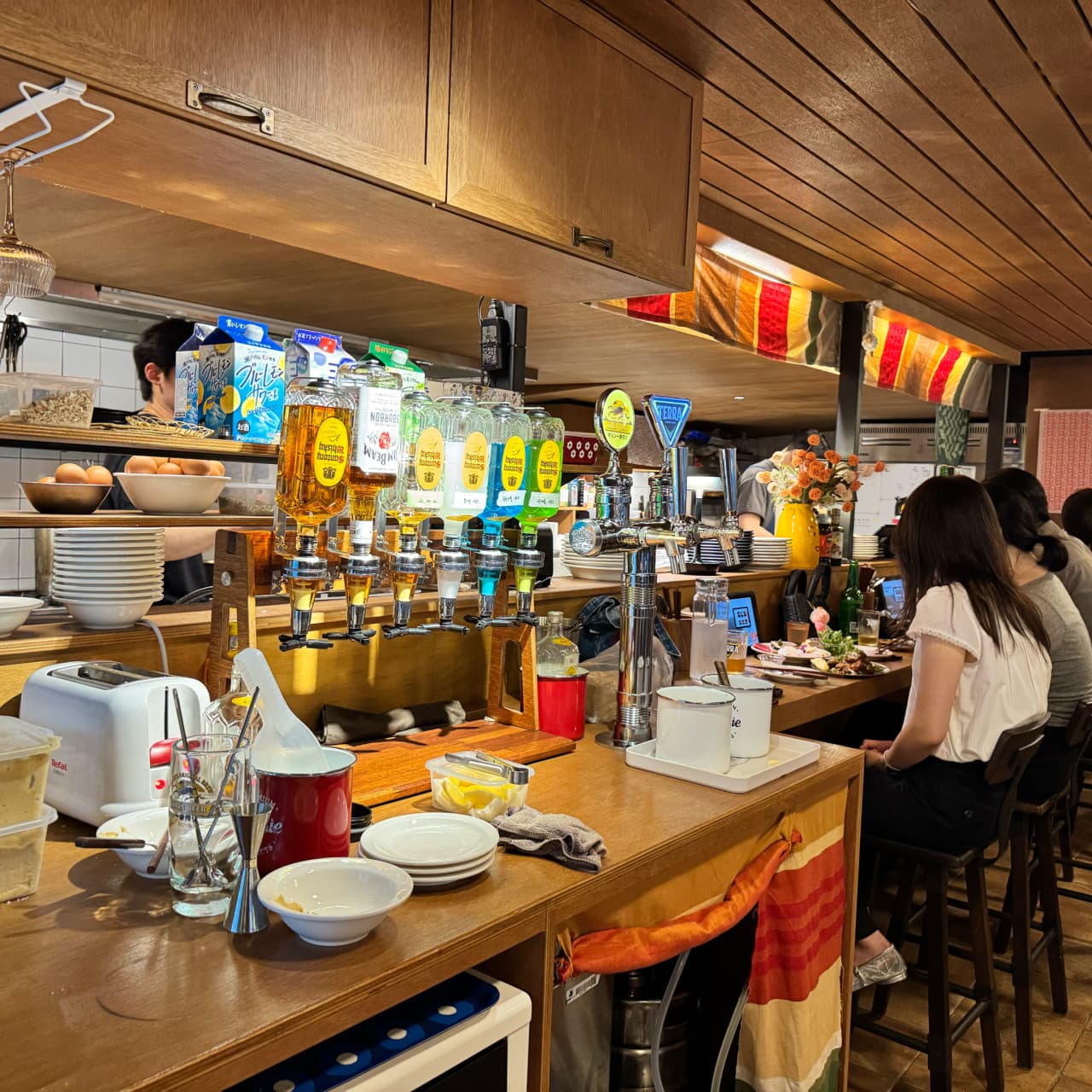 인천광역시 남동구 이자카야 쇼텐 구월점 인천의 나무 다찌석과 하이볼 디스펜서. 노란 조명 아래 카운터석에서 혼술을 즐기는 상황.