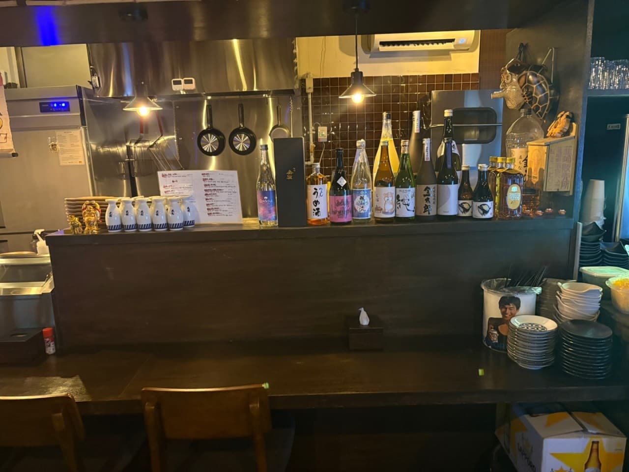 부산광역시 동구 이자카야 아지센 초량의 나무 다찌석. 노란 조명 아래 사케 병과 식기가 정돈된 카운터에서 즐기는 1인 혼술 공간.