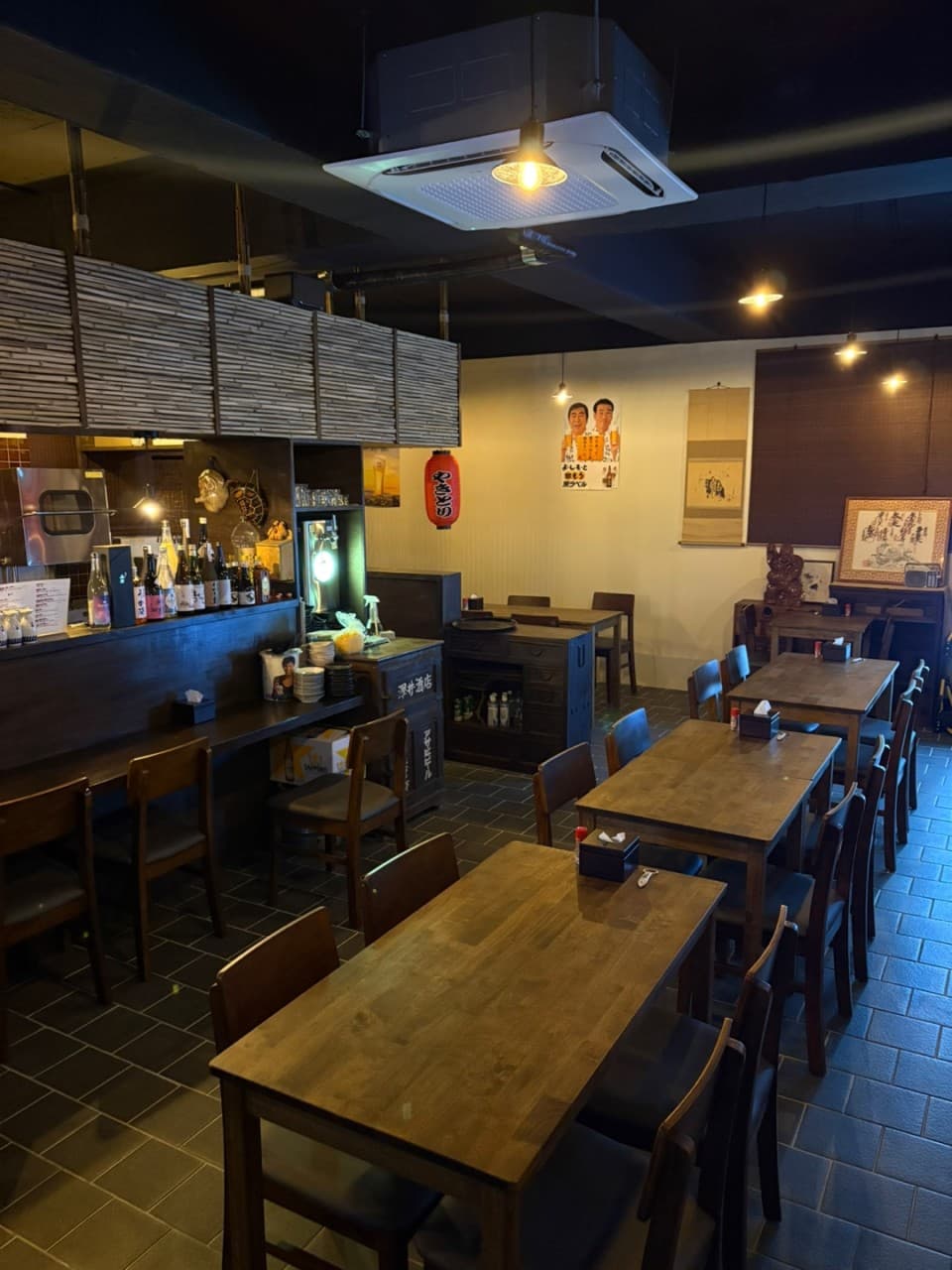 부산광역시 동구 이자카야 아지센 초량. 주황색 펜던트 조명 아래 배치된 목재 테이블과 1인 다찌석. 사케 병이 진열된 카운터와 일본식 소품이 어우러진 혼술 공간.