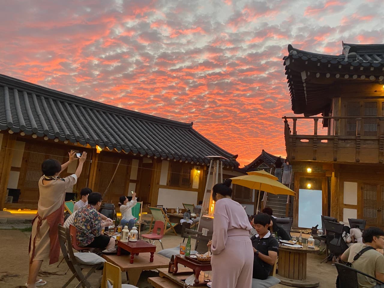 경상북도 경주시 황남거북이 경주 맥주 호프 - 붉은 노을과 히터 조명 아래 한옥 마당 1인 소반에서 혼술하며 병맥주를 마시는 상황