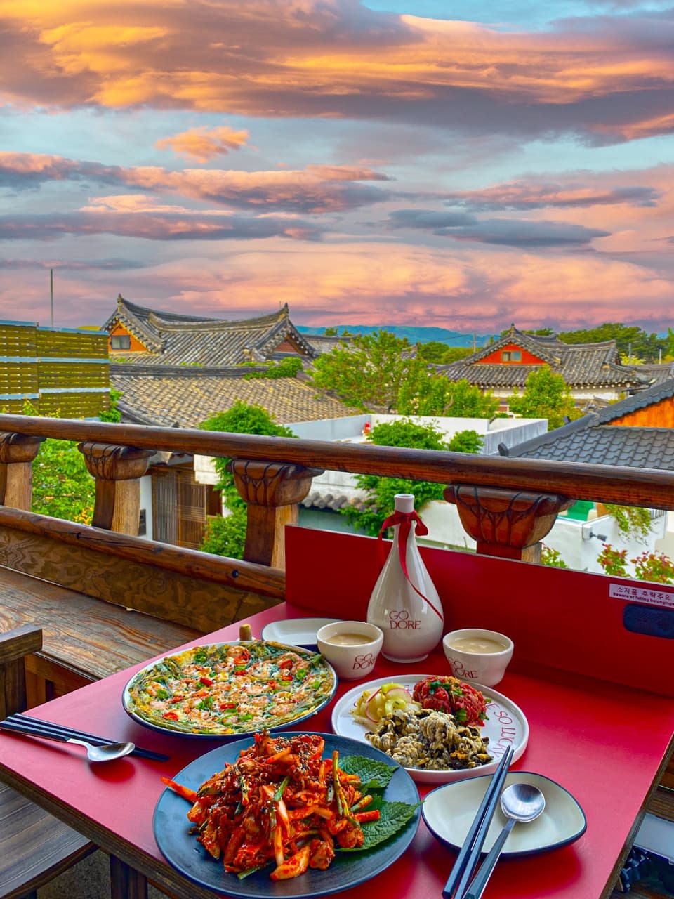 경상북도 경주시 고도리 경주 요리주점 테라스 좌석. 노을 아래 한옥 지붕 배경으로 해물파전과 육회, 전통주가 차려진 1인 혼술 상차림.