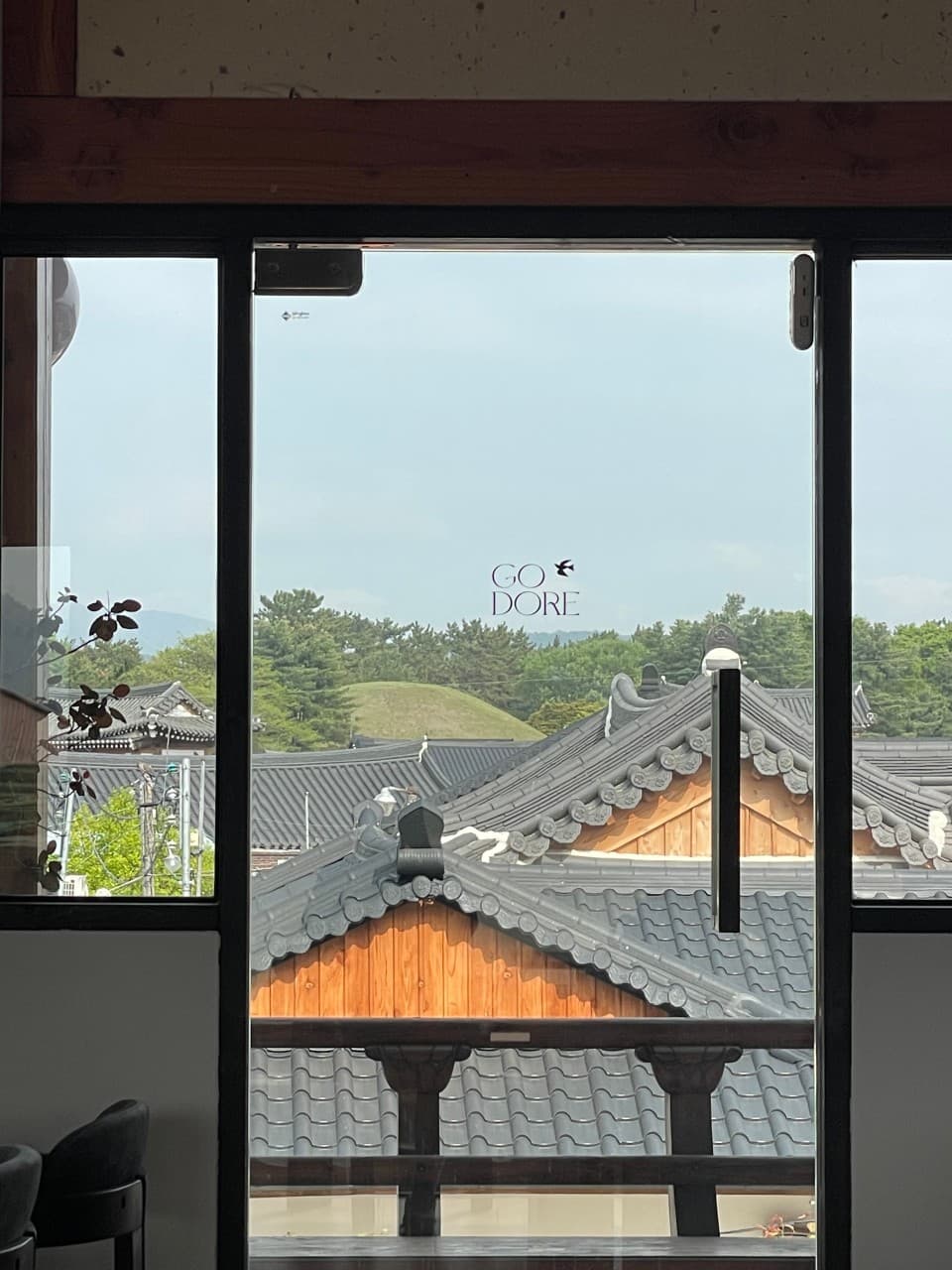 경상북도 경주시 요리주점 고도리 경주 창가 1인 다찌석. 통유리 너머 한옥 기와와 고분 능선이 보이는 배경에서 즐기는 혼술 상황 묘사.