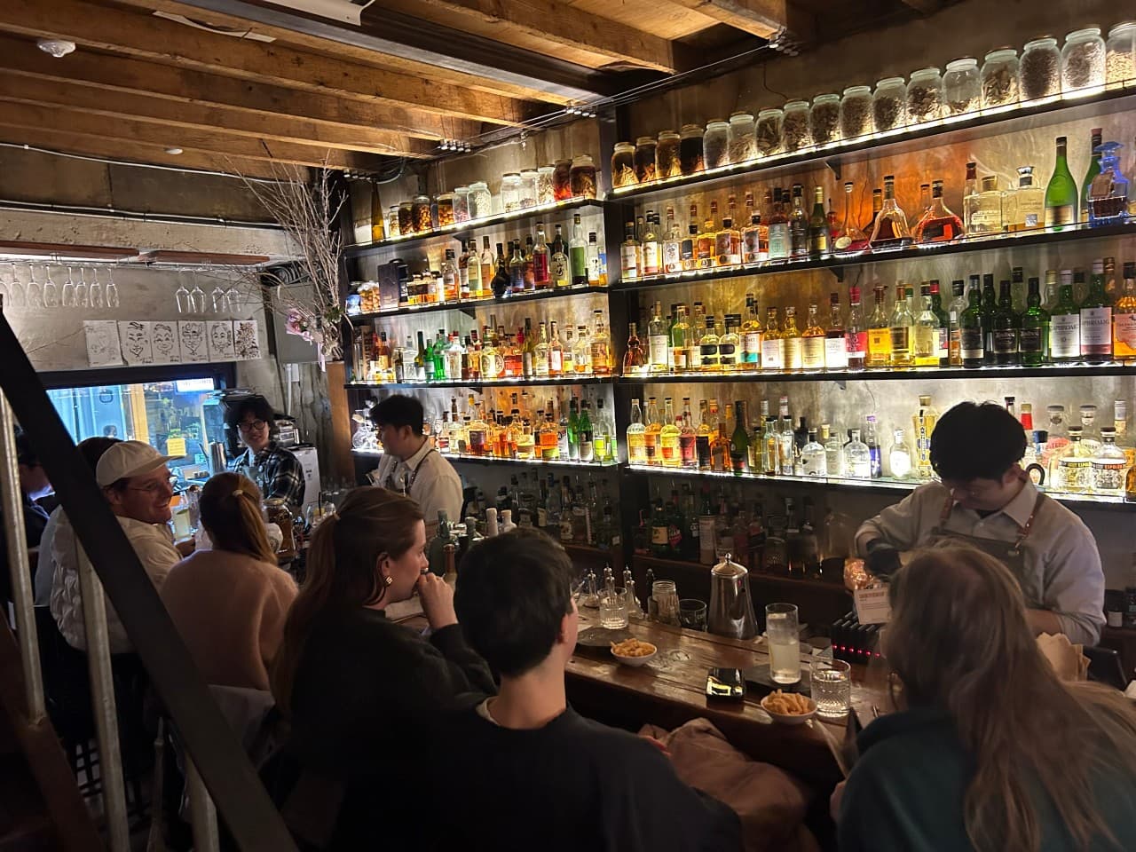 경상북도 경주시 BAR분 경주 바(Bar) 내부. 노란 조명 아래 진열된 다양한 술병과 나무 다찌석에 앉은 1인 손님들이 혼술을 즐기는 상황.