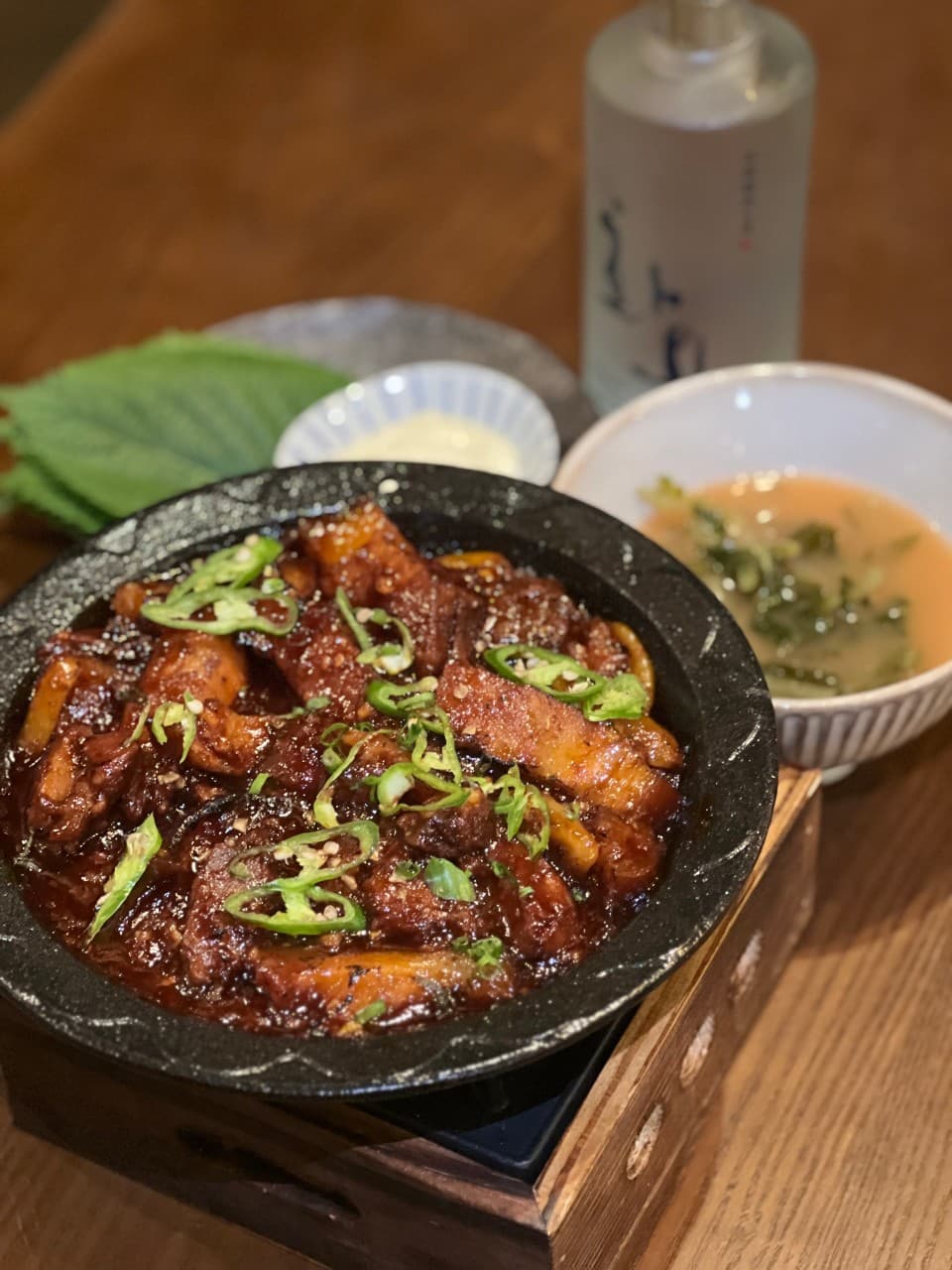 경상북도 경주시 이자카야 범굴 경주 다찌석. 매콤한 고기 요리와 깻잎, 전통주가 차려진 1인 혼술 상황. 따뜻한 색 조명 아래 나무 테이블과 음식의 질감을 강조.