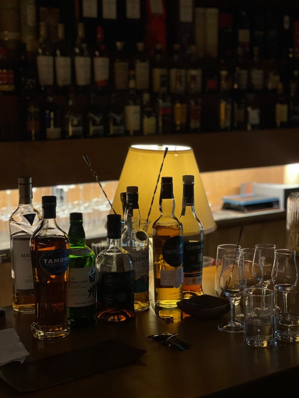 경상북도 경주시 라지백 경주 바(Bar)의 노란 스탠드 조명 아래 진열된 위스키 병과 글라스. 1인 다찌석에서 혼술을 즐기는 상황을 묘사함.