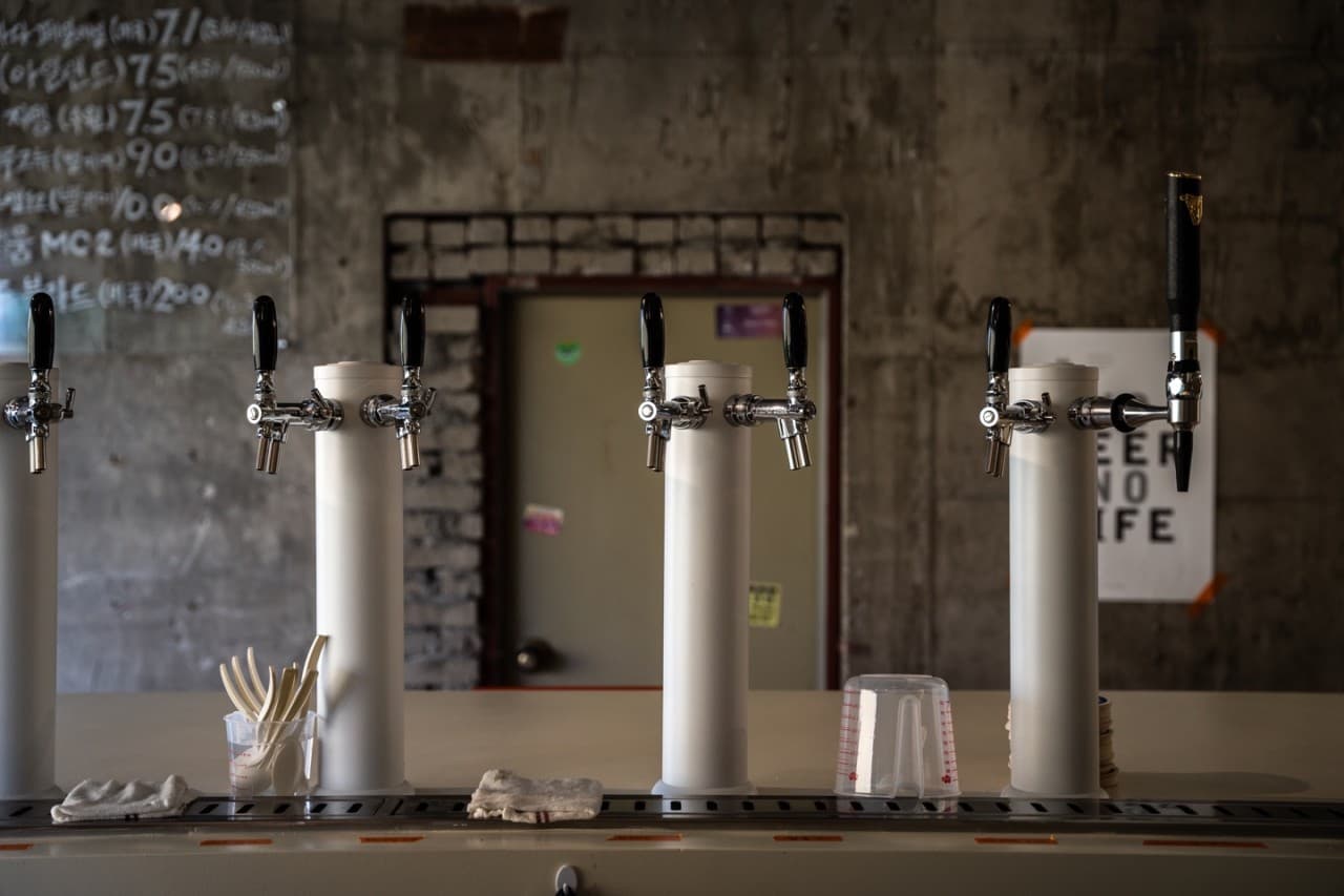 경상북도 경주시 흐흐흐 경주 맥주 호프 다찌석에 일렬로 배치된 화이트 맥주 탭과 노출 콘크리트 벽면. 1인 혼술을 위한 카운터 바 테이블 위 정돈된 식기류.
