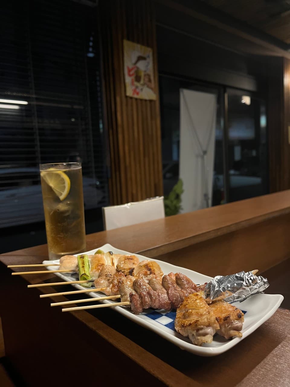 경상북도 경주시 이자카야 토리우 경주 혼술 다찌석. 나무 카운터 위 노릇하게 구워진 닭꼬치와 레몬 하이볼 한 잔이 놓인 1인 식사 상황. 어두운 실내 조명과 목재 벽면이 대비되는 분위기.