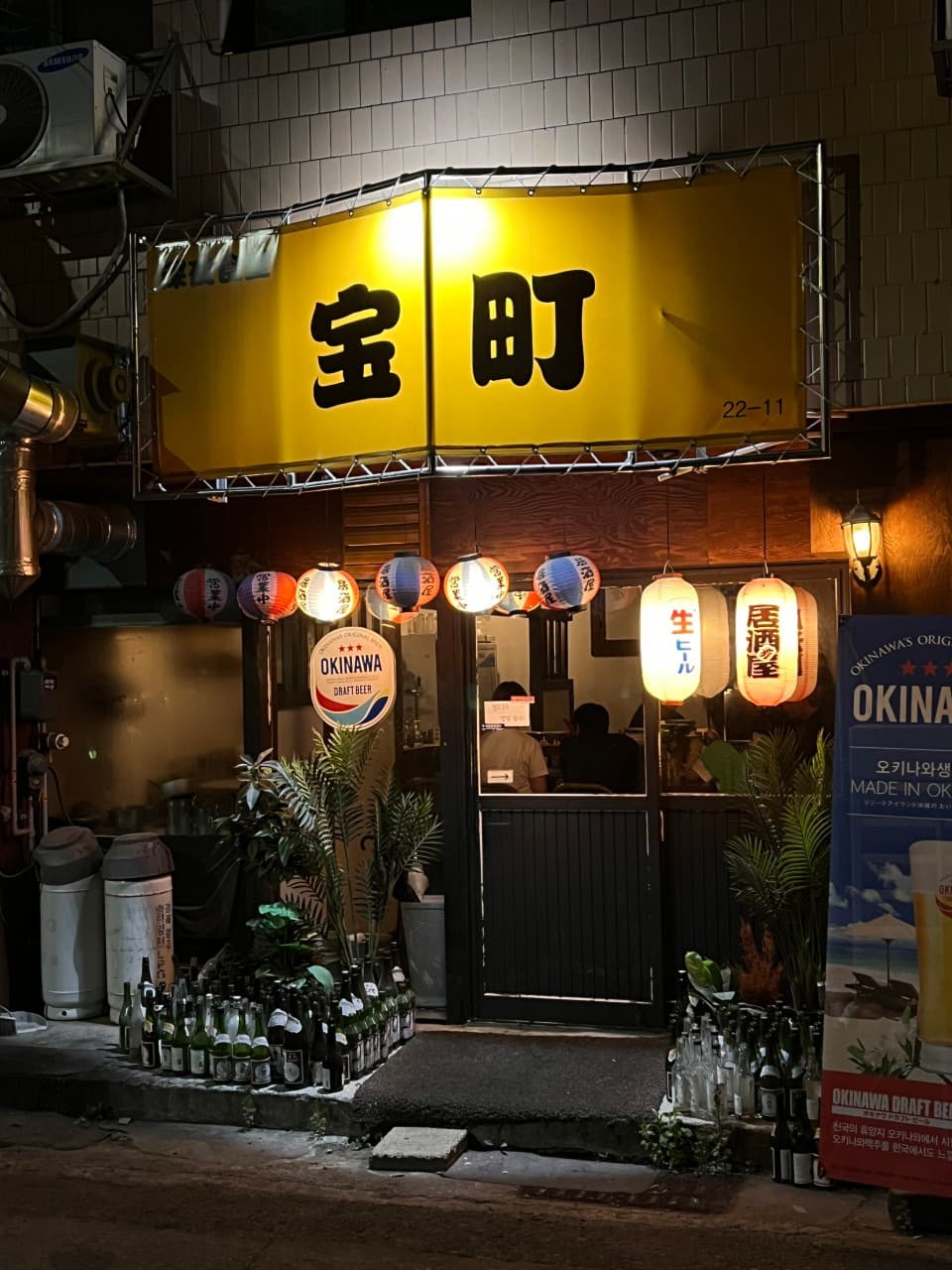 경상북도 경주시 다카라초 경주 이자카야의 노란 간판과 제등 조명. 입구에 나열된 술병들과 내부 다찌석이 보이는 외관에서 혼술을 즐기는 상황.