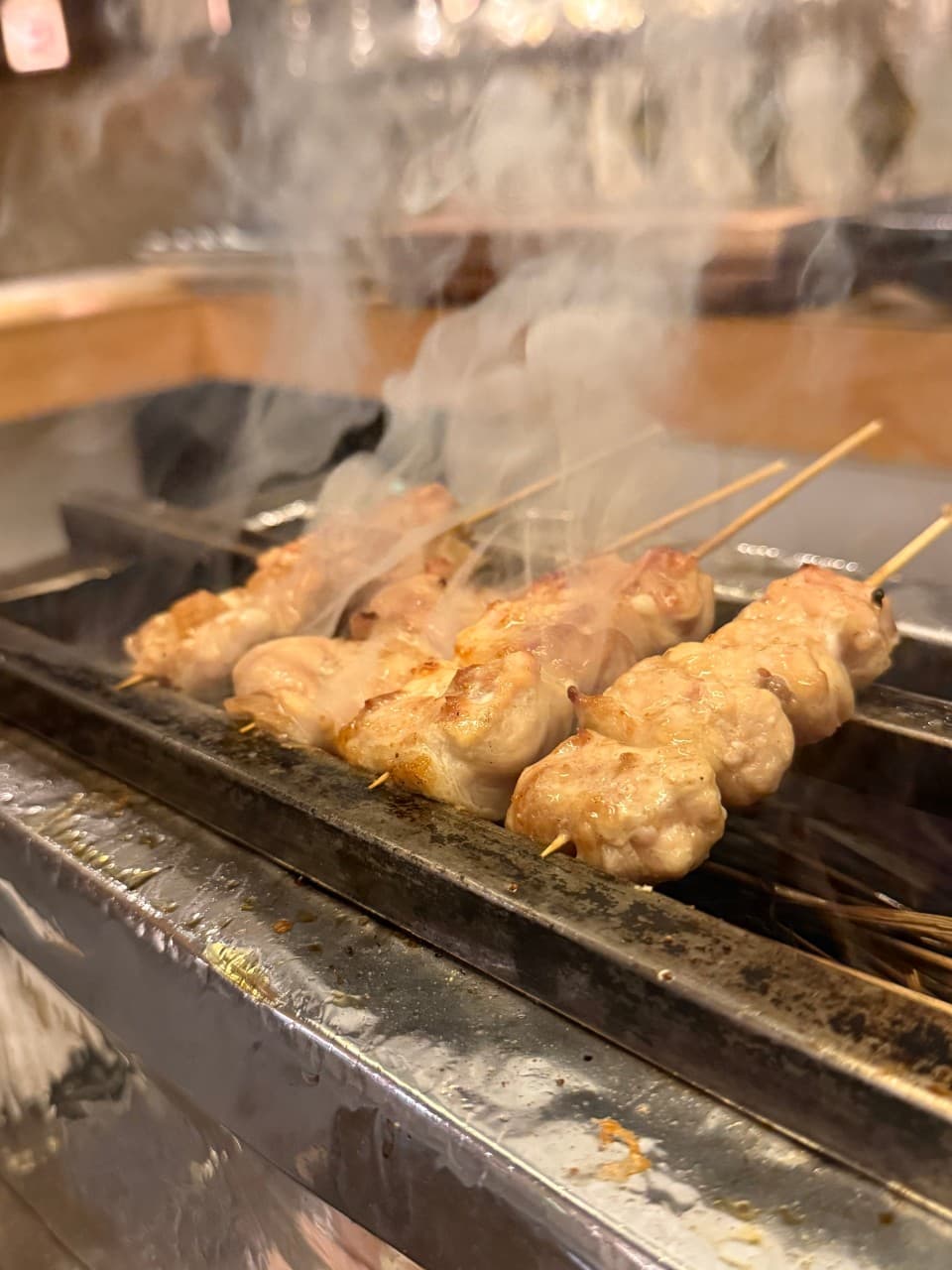 경상북도 경주시 코토리 경주 이자카야 다찌석에서 즐기는 1인 꼬치구이. 연기가 피어오르는 노릇한 닭꼬치 질감과 주황빛 조명 아래 혼술 상황.