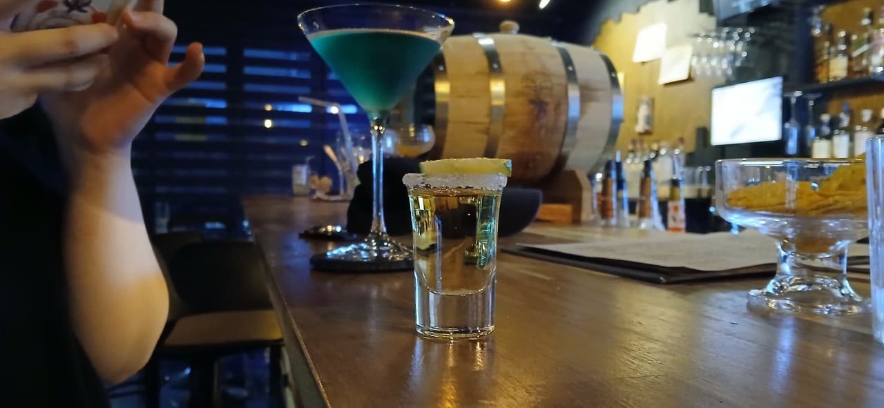 경상북도 경주시 혼술 바 페인터 닷츠 경주 - 목재 다찌석 위 레몬 샷잔과 푸른 칵테일. 노란 조명 아래 1인 카운터석에서 술을 마시는 상황