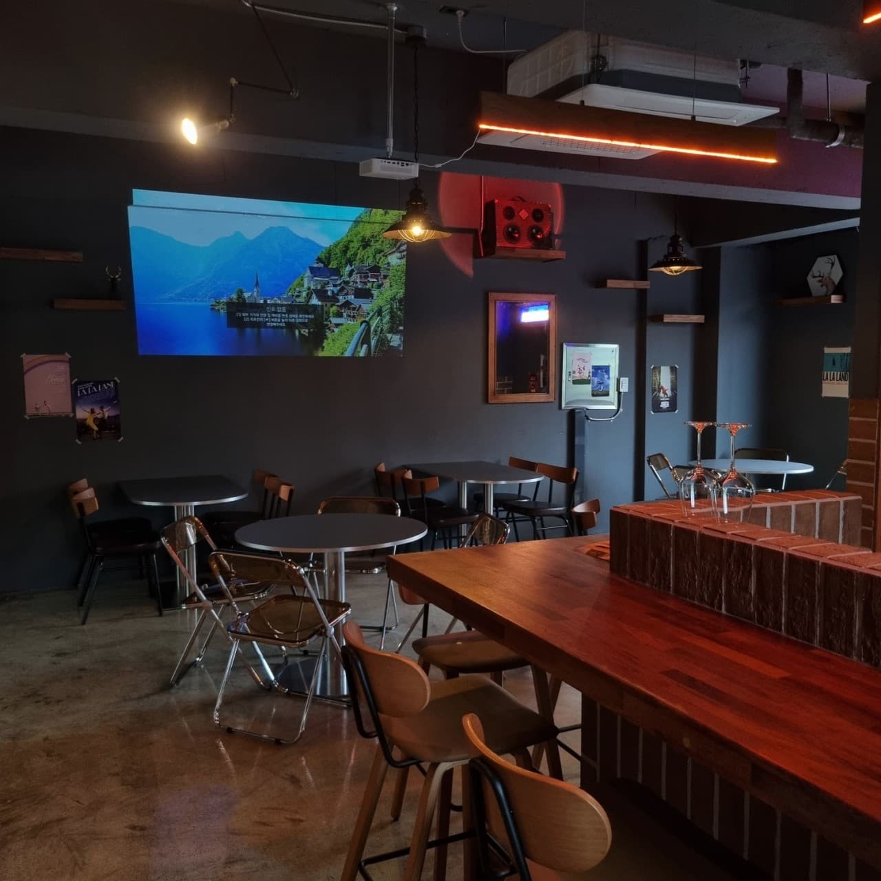 경상북도 포항시 요리주점 사슴 포항의 핀 조명 아래 원목 다찌석과 1인용 좌석이 배치된 실내. 벽면 스크린 영상이 투사되는 어두운 공간에서 혼술을 하는 상황.