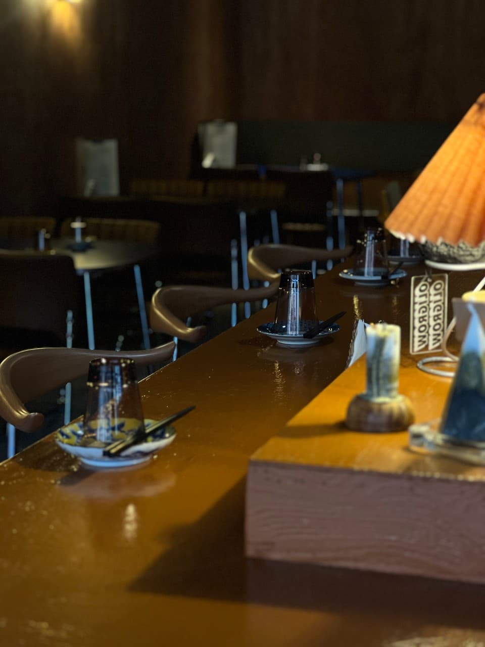 경상북도 포항시 잔잔바리 포항 요리주점 - 주황색 조명이 비치는 나무 다찌석에 유리잔과 앞접시가 세팅된 1인 혼술 공간