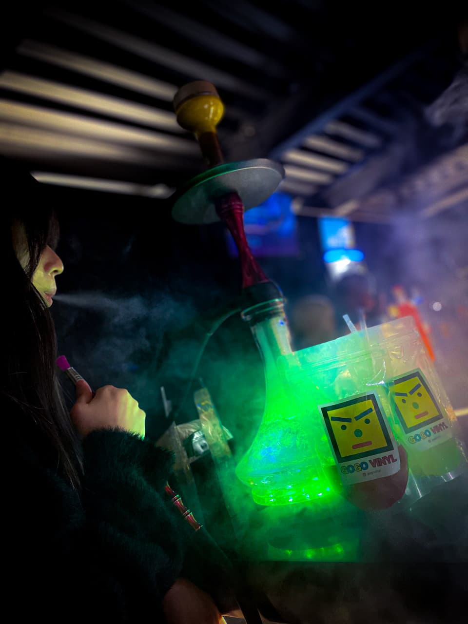 대구광역시 중구 고고비닐 대구 1인 혼술 와인 바 - 초록색 네온 조명 아래 다찌석에서 비닐 파우치 음료와 후카 연기가 어우러진 상황