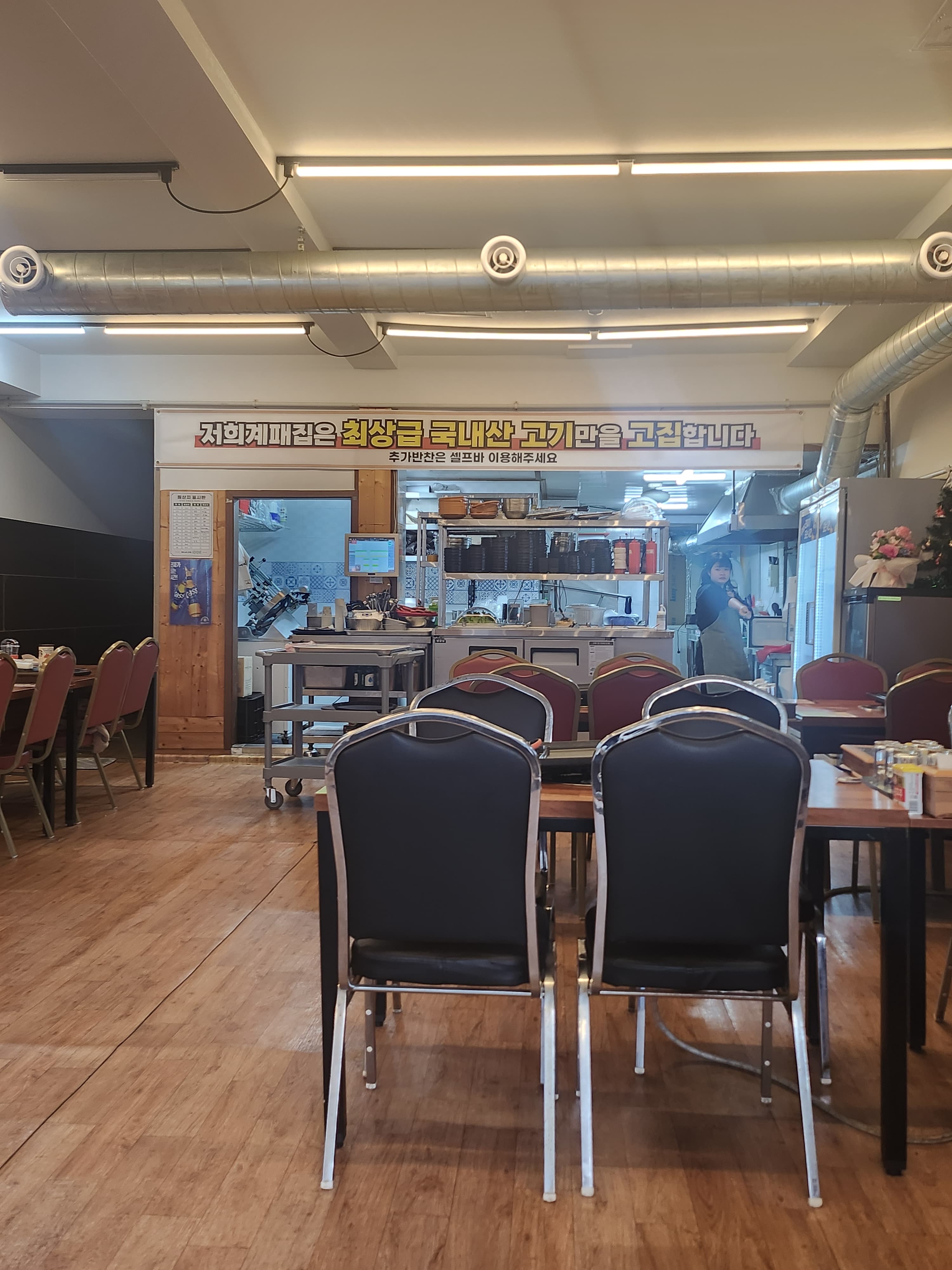 전라남도 목포시 목포 계패집 혼밥 식당 - 밝은 조명 아래 원목 바닥과 테이블이 배치된 내부. 주방 위로 국내산 고기 안내 현수막이 걸린 정돈된 분위기
