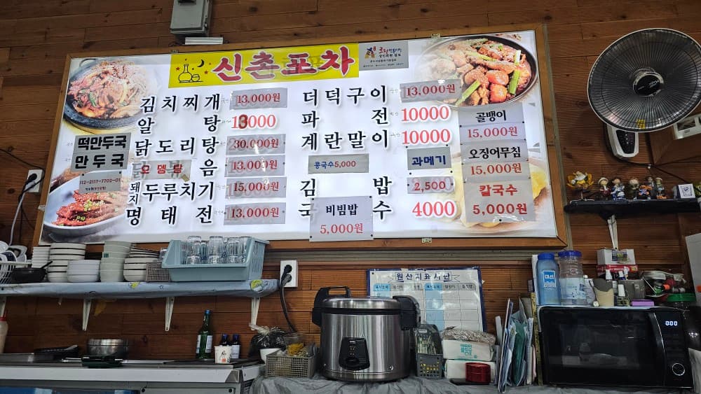 부산광역시 동구 신촌포차 초량 포장마차 주방 나무 벽면의 메뉴판. 김치찌개와 파전 등 안주 가격표 아래로 밥솥과 전자레인지가 놓인 1인 혼술 식당의 내부 풍경
