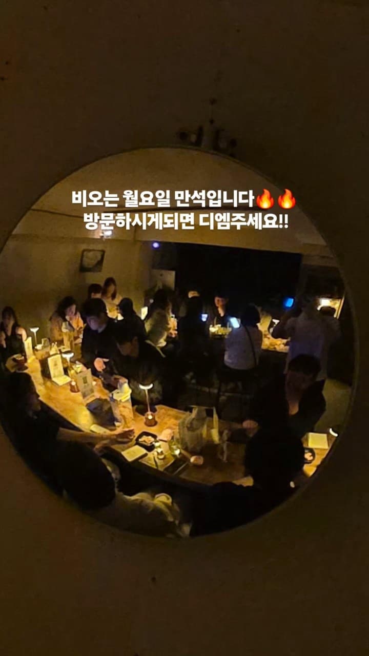 경기도 의정부시 제주도트 혼술바 의정부점 바(Bar). 어두운 조명 아래 긴 나무 다찌석과 개별 조명이 있는 1인 좌석. 거울 너머 비오는 월요일 만석인 매장에서 혼술을 즐기는 상황.